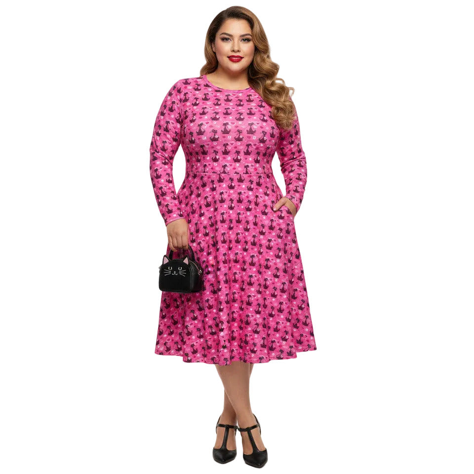 Plus size woman wearing a pink long sleeve vintage 1950s dress with cat print and functional side pockets.