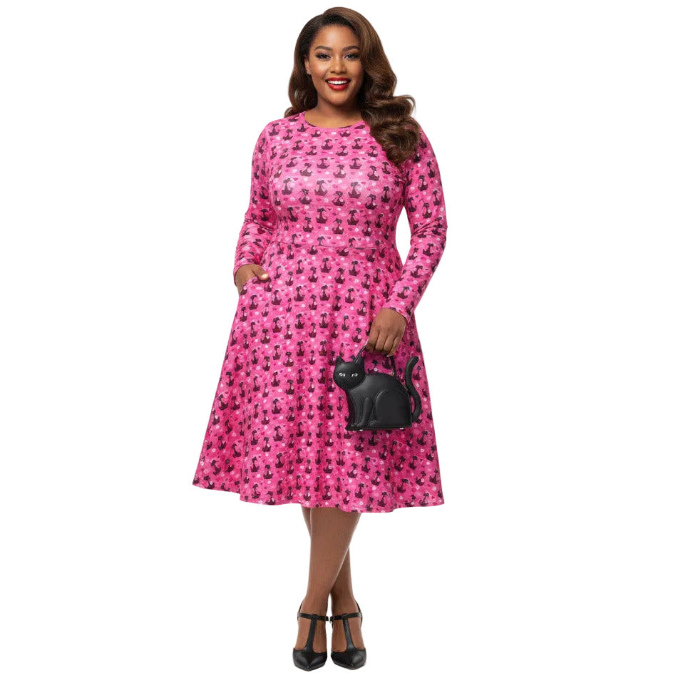 Plus size woman wearing a pink retro-style long sleeve vintage 1950s dress with cat print and functional side pockets.