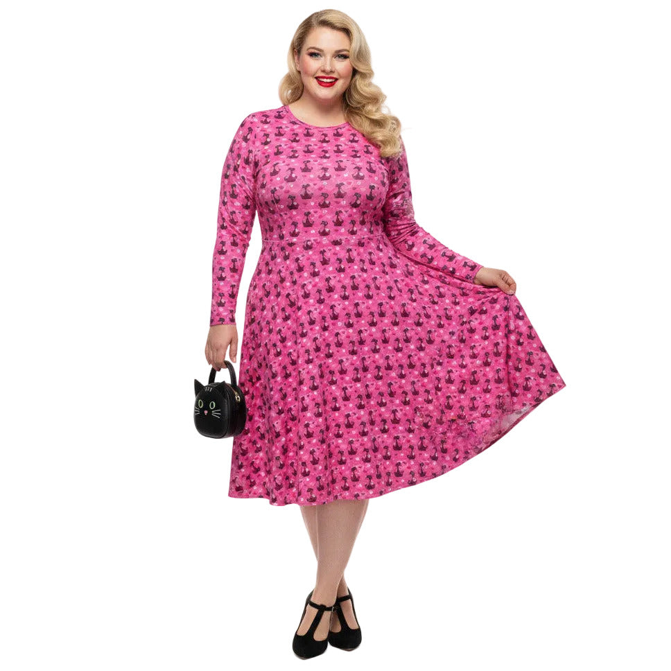 Woman wearing a pink long sleeve vintage-inspired 1950s dress with cat print and functional side pockets.