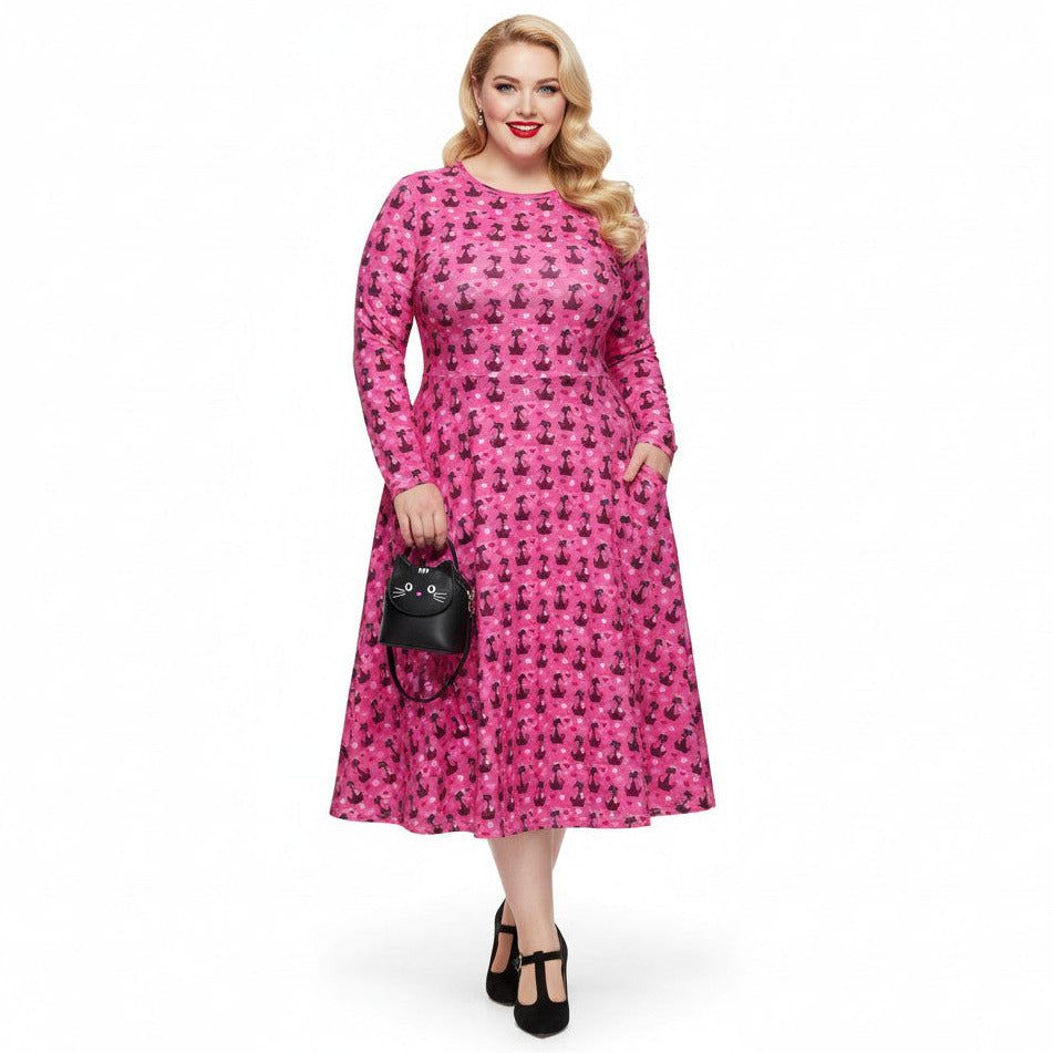 Plus size woman wearing a pink retro-style long sleeve vintage 1950s dress with cat print and functional side pockets.
