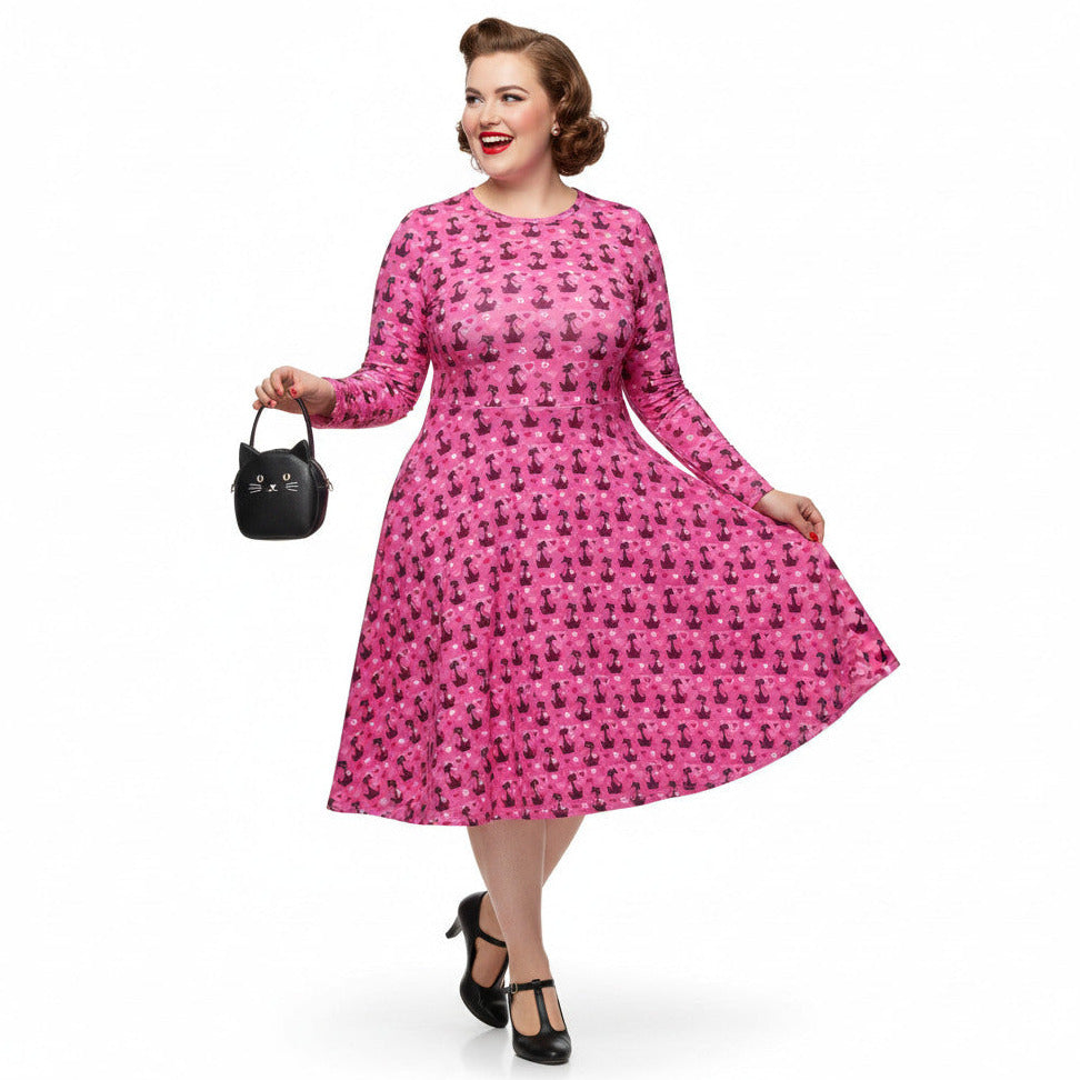 Woman wearing a pink long sleeve vintage-inspired 1950s dress with cat print and functional side pockets.