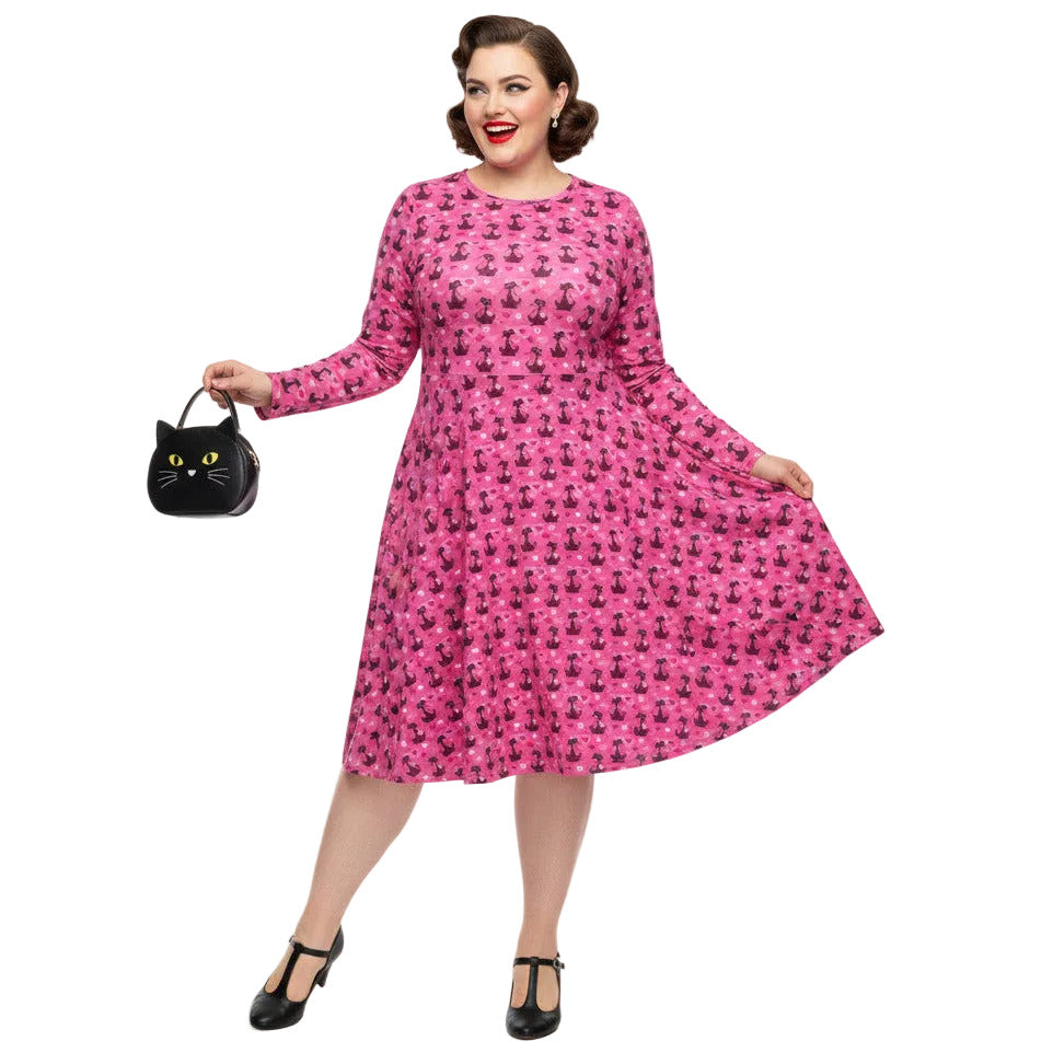 Woman wearing a pink long sleeve vintage-inspired 1950s dress with cat print and functional side pockets.