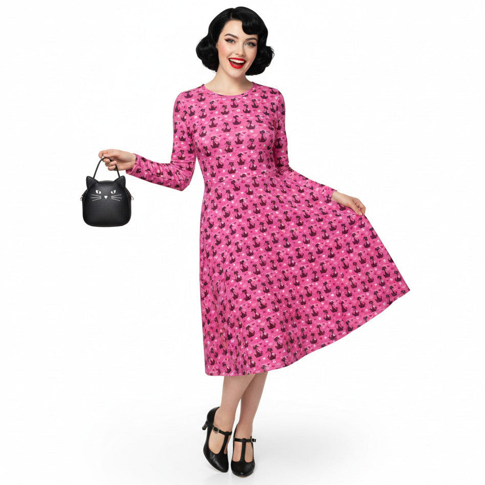 Woman wearing a pink long sleeve vintage-inspired 1950s dress with cat print and functional side pockets.