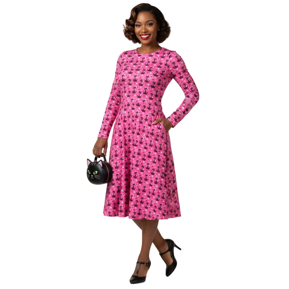 Woman wearing a pink long sleeve vintage-inspired 1950s dress with cat print and functional side pockets.
