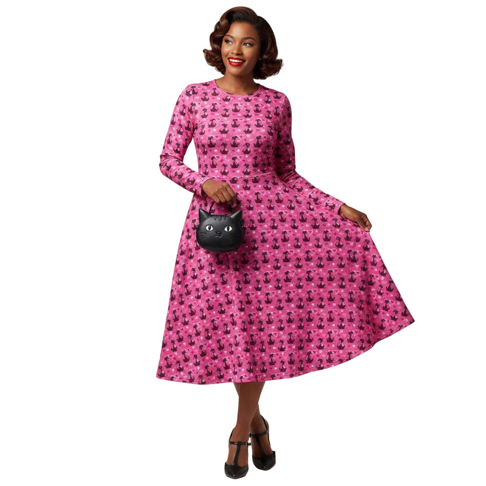 Woman wearing a pink long sleeve vintage-inspired 1950s dress with cat print and functional side pockets.
