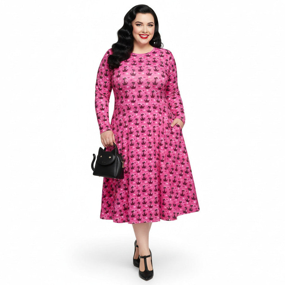 Plus Size Woman wearing a pink long sleeve vintage-inspired 1950s dress with cat print and functional side pockets.