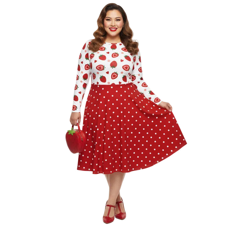 Plus size woman wearing a long sleeve white and red strawberry pin-up swing dress with red polka dot skirt and pockets.