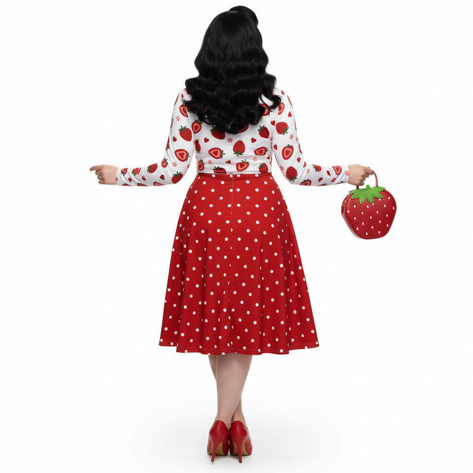 woman wearing a long sleeve white and red strawberry pin-up swing dress with red polka dot skirt and pockets.