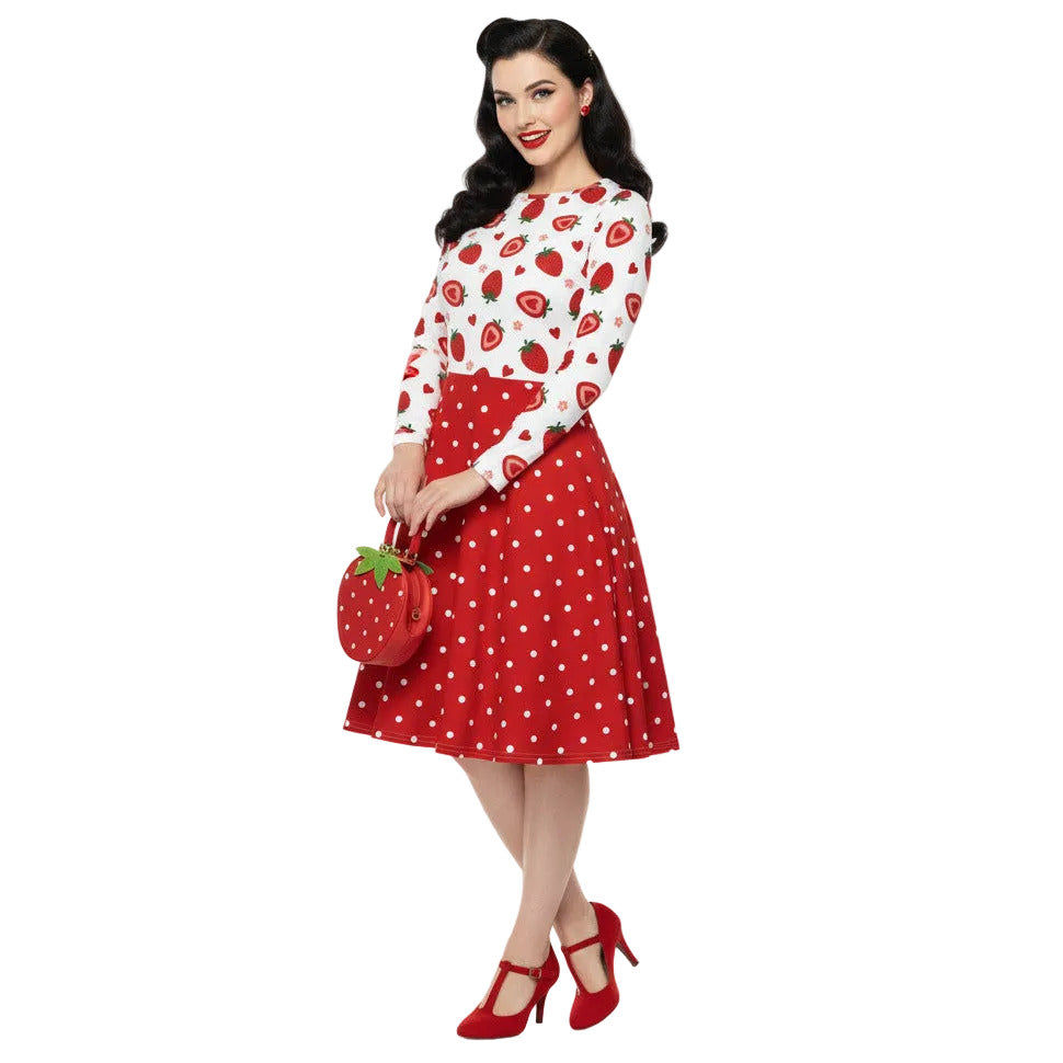 woman wearing a long sleeve white and red strawberry pin-up swing dress with red polka dot skirt and pockets.