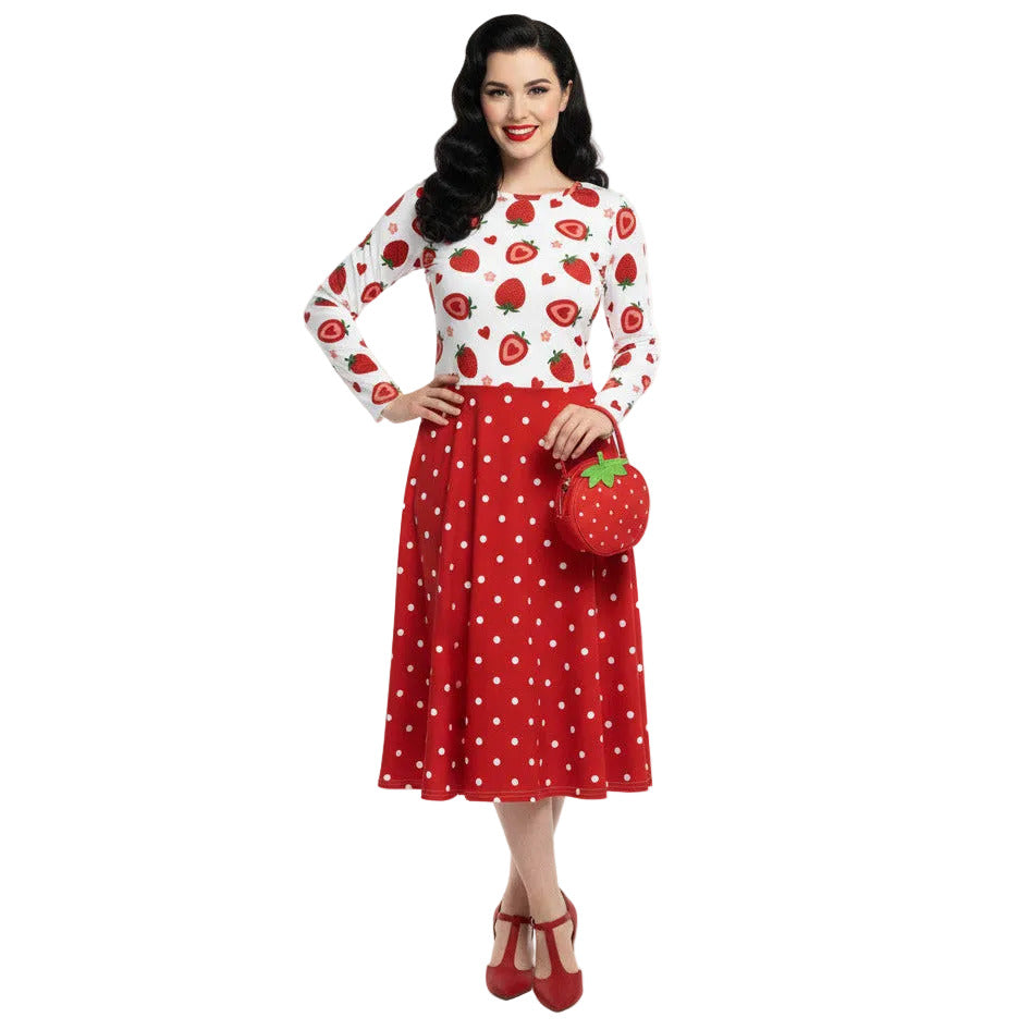 woman wearing a long sleeve white and red strawberry pin-up swing dress with red polka dot skirt and pockets.