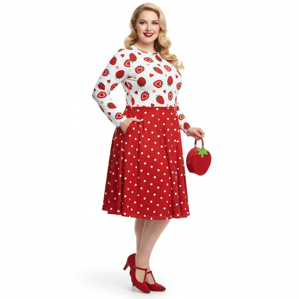 Plus size woman wearing a long sleeve white and red strawberry pin-up swing dress with red polka dot skirt and pockets.