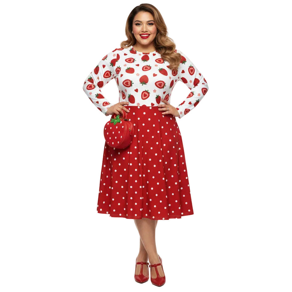 Plus size woman wearing a long sleeve white and red strawberry pin-up swing dress with red polka dot skirt and pockets.