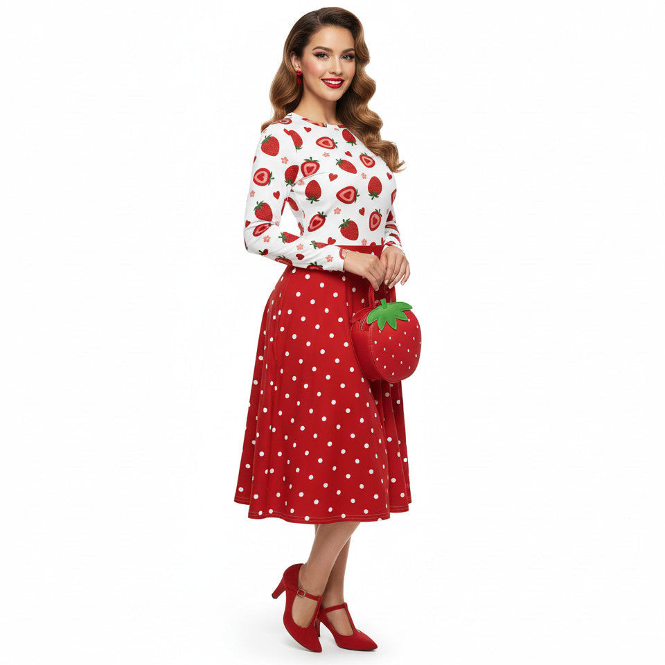 woman wearing a long sleeve white and red strawberry pin-up swing dress with red polka dot skirt and pockets.