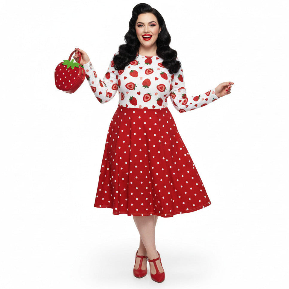Plus size woman wearing a long sleeve white and red strawberry pin-up swing dress with red polka dot skirt and pockets.