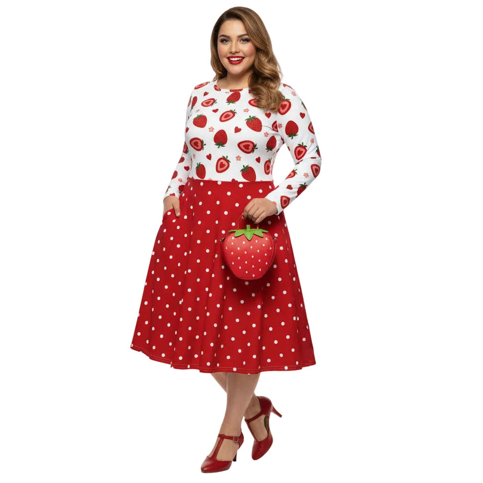 Plus size woman wearing a long sleeve white and red strawberry pin-up swing dress with red polka dot skirt and pockets.