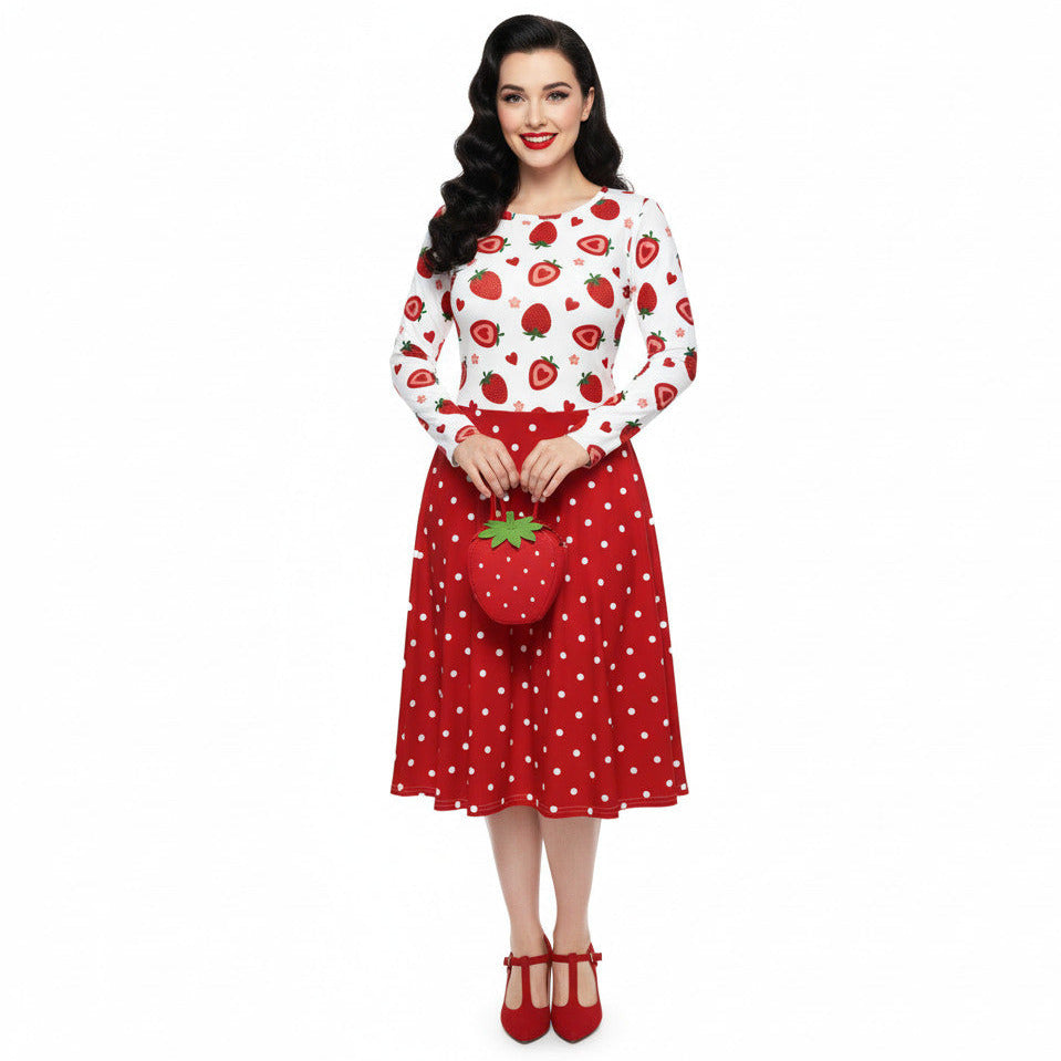 woman wearing a long sleeve white and red strawberry pin-up swing dress with red polka dot skirt and pockets.