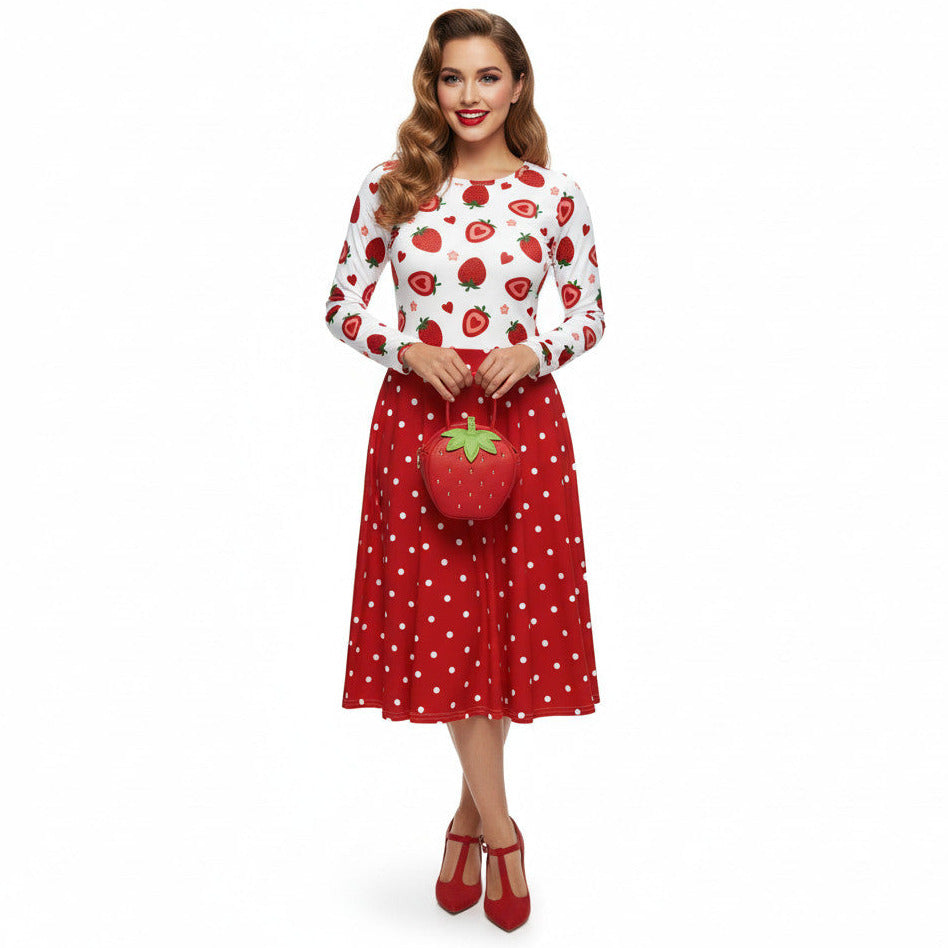 woman wearing a long sleeve white and red strawberry pin-up swing dress with red polka dot skirt and pockets.
