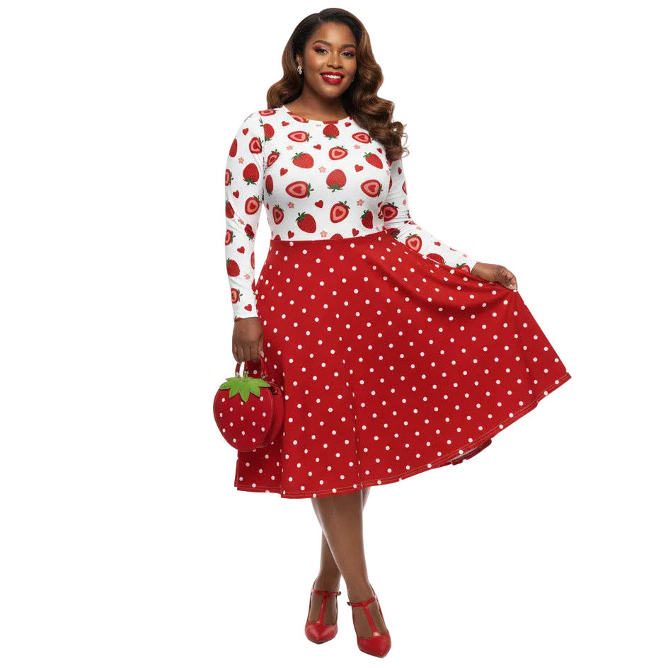 Plus size woman wearing a long sleeve white and red strawberry pin-up swing dress with red polka dot skirt and pockets.