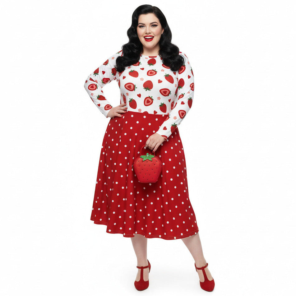 Plus size woman wearing a long sleeve white and red strawberry pin-up swing dress with red polka dot skirt and pockets.