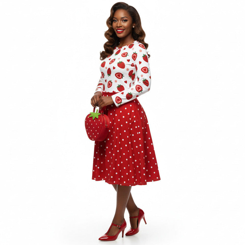 woman wearing a long sleeve white and red strawberry pin-up swing dress with red polka dot skirt and pockets.