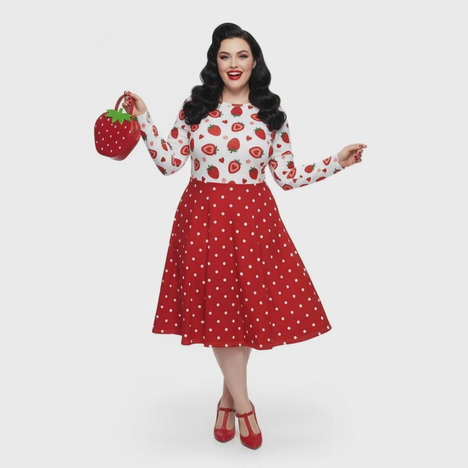 Plus size woman wearing a long sleeve white and red strawberry pin-up swing dress with red polka dot skirt and pockets.