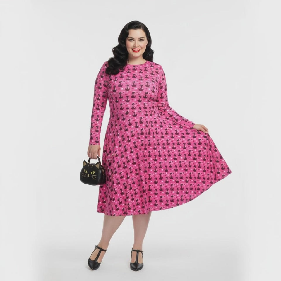 Plus size woman wearing a pink retro-style long sleeve vintage 1950s dress with cat print and functional side pockets.