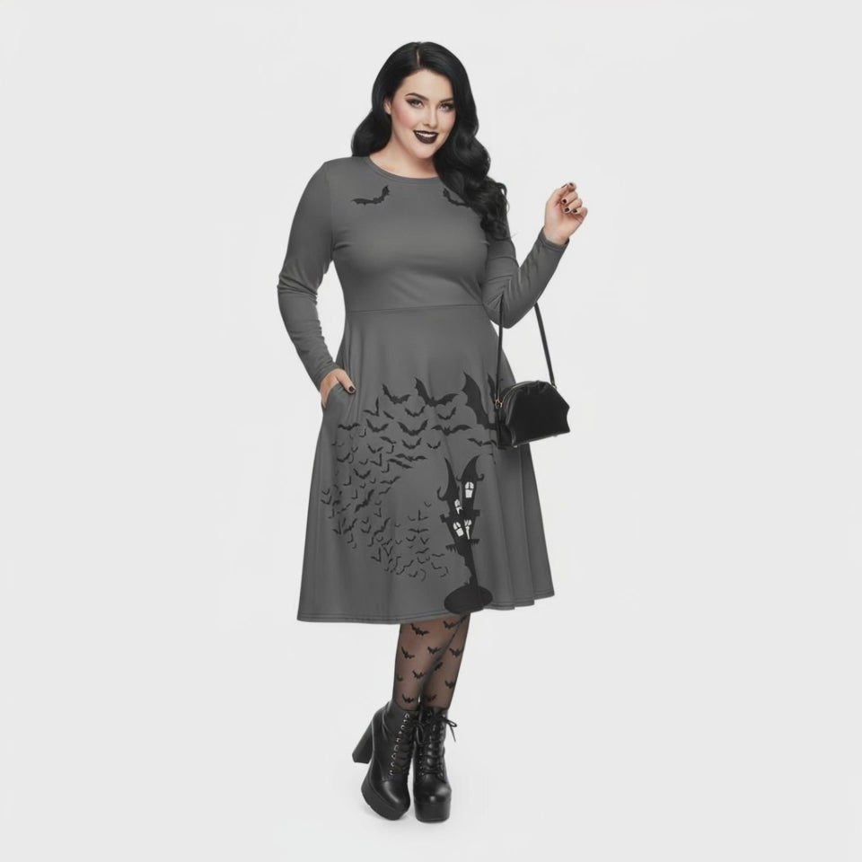 Plus size woman wearing a grey long sleeve goth pinup dress with black bat and haunted house print featuring functional side pockets.