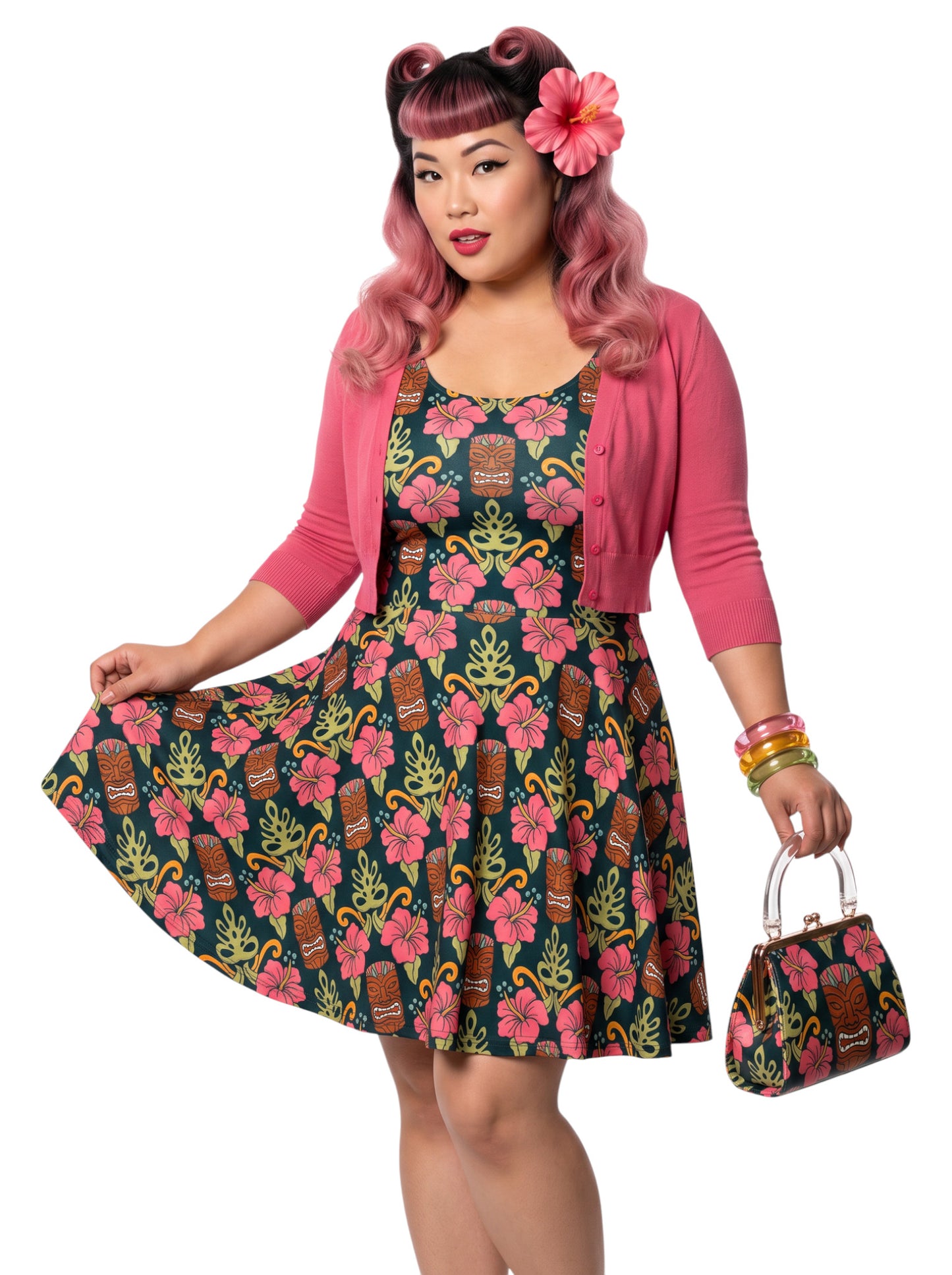 A plus size woman wearing a dark green 1950s-style pinup rockabilly swing dress with an all-over tropical print of tiki masks, pink hibiscus flowers, and monstera leaves. 