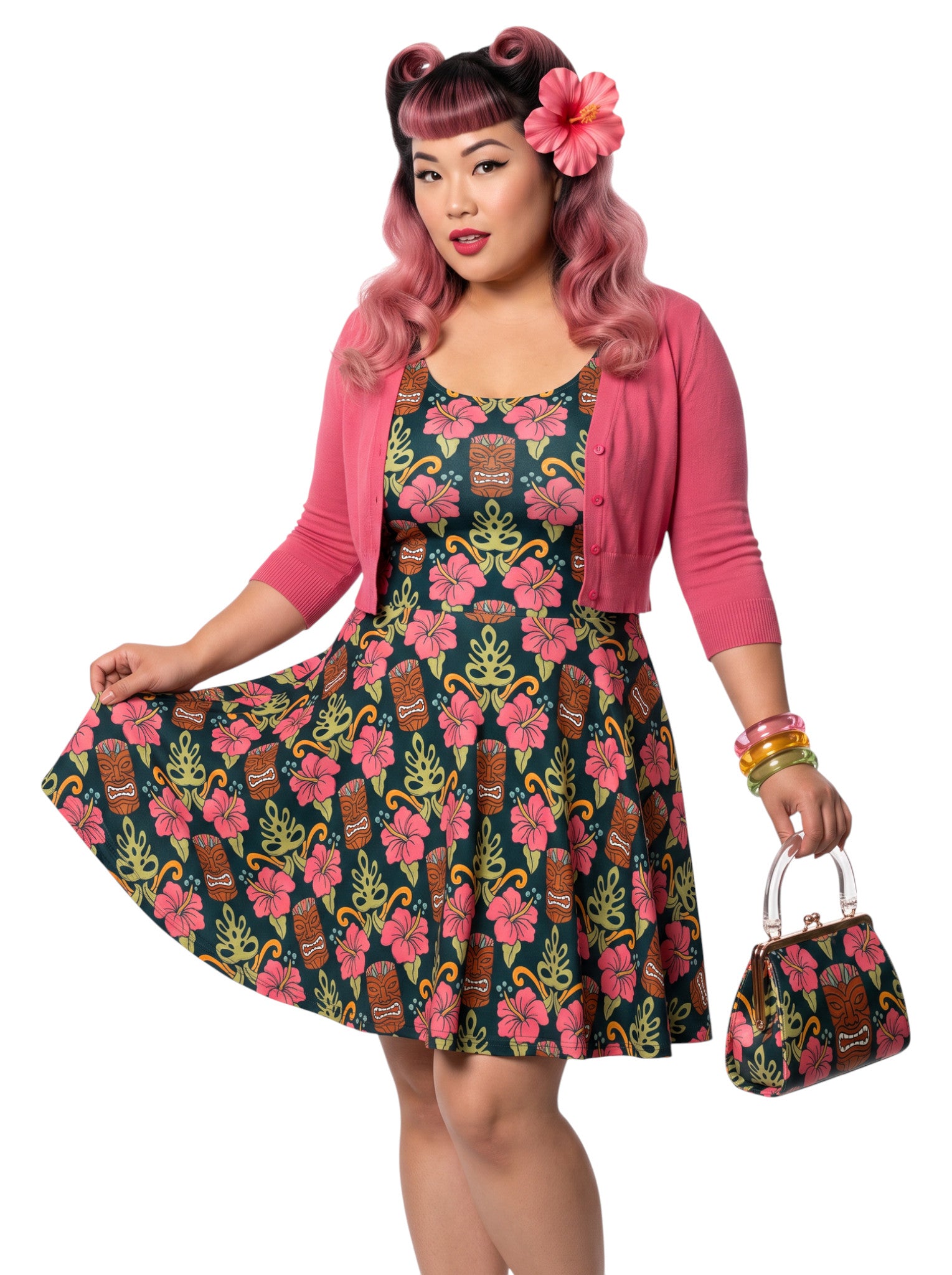 A plus size woman wearing a dark green 1950s-style pinup rockabilly swing dress with an all-over tropical print of tiki masks, pink hibiscus flowers, and monstera leaves. 