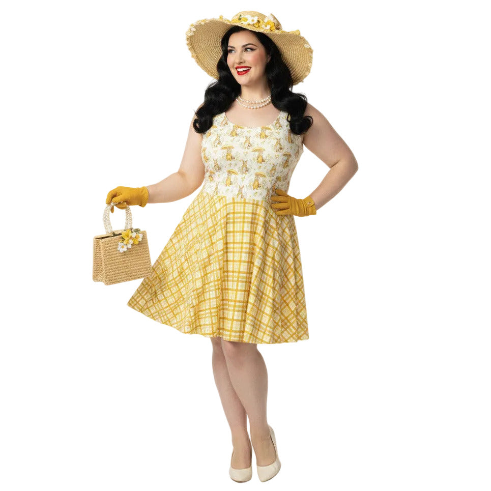 Plus size woman wearing a yellow gingham and Mr. Rabbit print 1950s vintage style fit and flare swing dress with straw hat.