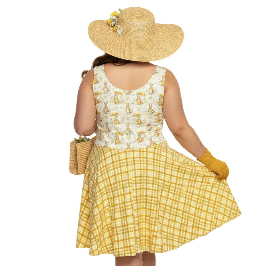 Plus size woman wearing a yellow gingham and Mr. Rabbit print 1950s vintage style fit and flare swing dress with straw hat.