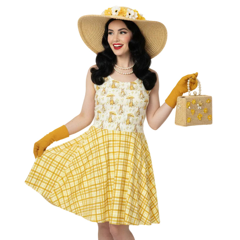 Woman wearing a yellow gingham and Mr. Rabbit print 1950s vintage style fit and flare swing dress with straw hat.