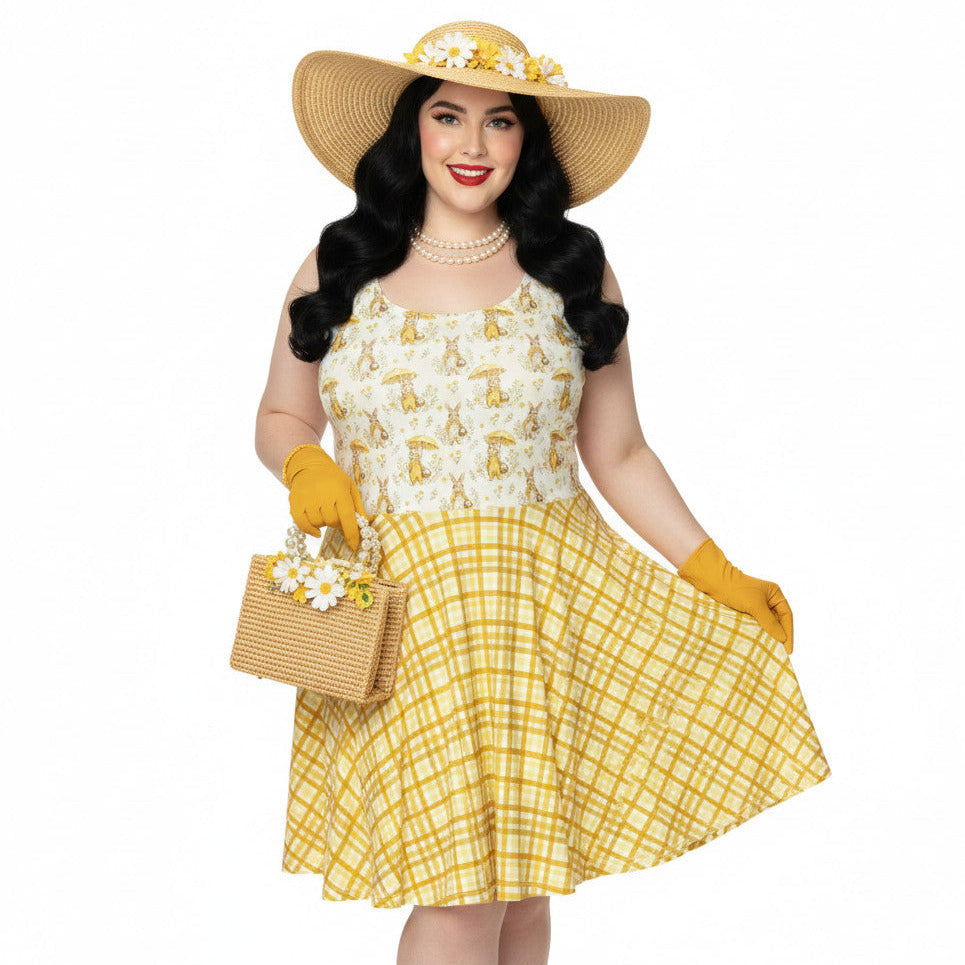 Plus size woman wearing a yellow gingham and Mr. Rabbit print 1950s vintage style fit and flare swing dress with straw hat.