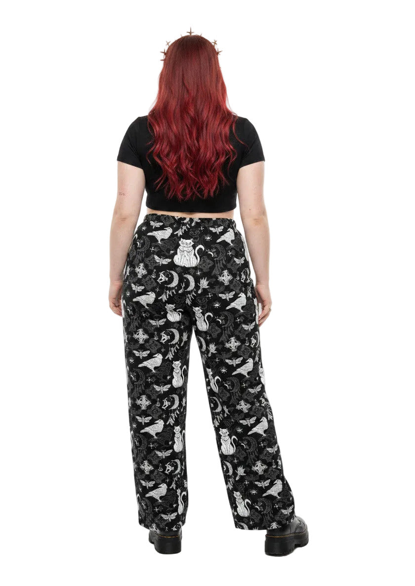 Woman wearing black wide-leg Whimsigoth lounge pants with white celestial cat and moon print.