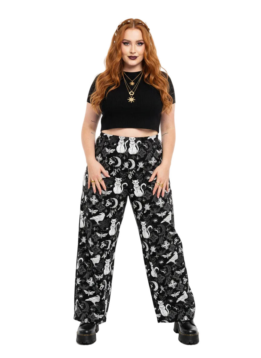 Woman wearing black wide-leg Whimsigoth lounge pants with white celestial cat and moon print.