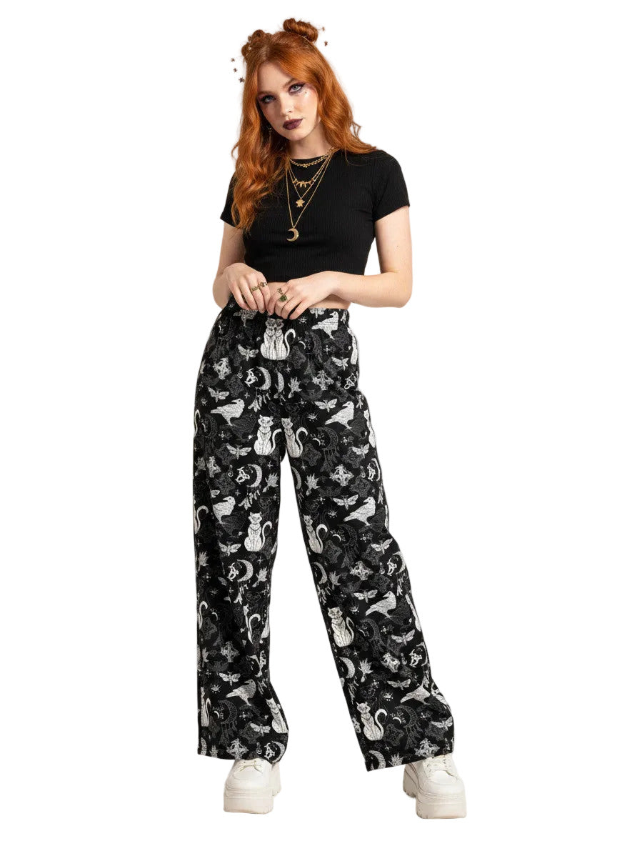 Woman wearing black wide-leg Whimsigoth lounge pants with white celestial cat and moon print.