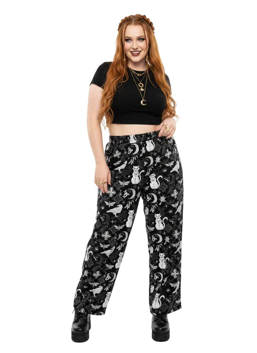 Woman wearing black wide-leg Whimsigoth lounge pants with white celestial cat and moon print.