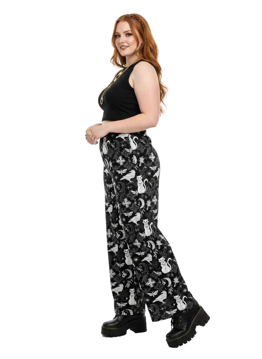 Woman wearing black wide-leg Whimsigoth lounge pants with white celestial cat and moon print.