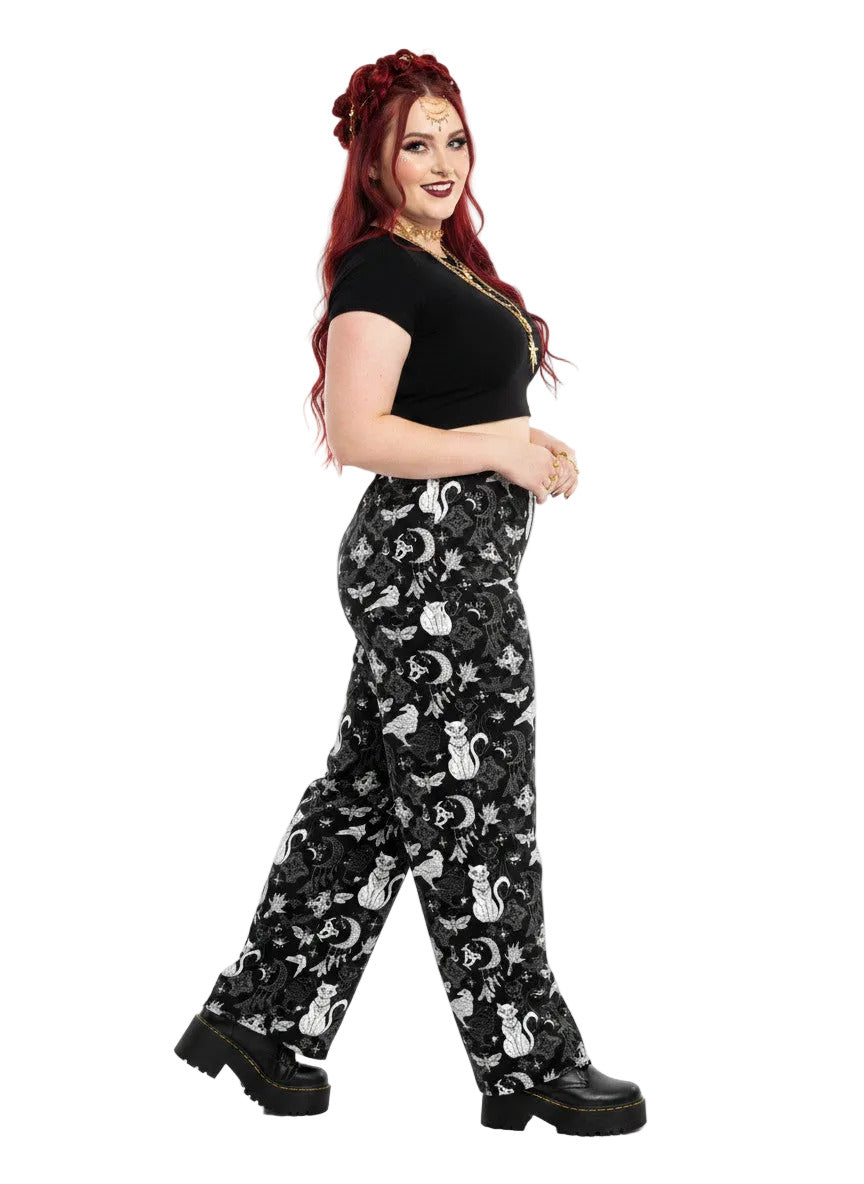 Woman wearing black wide-leg Whimsigoth lounge pants with white celestial cat and moon print.