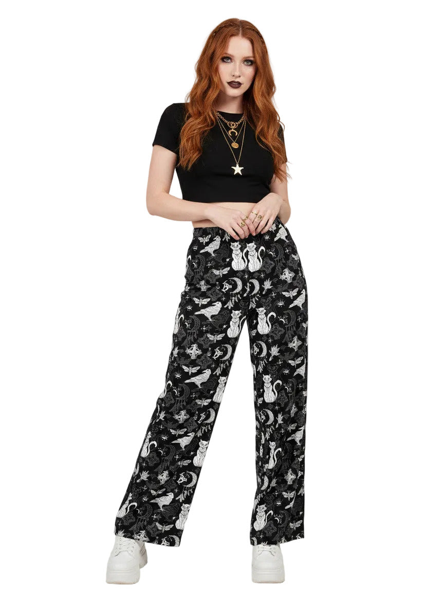 Woman wearing black wide-leg Whimsigoth lounge pants with white celestial cat and moon print.