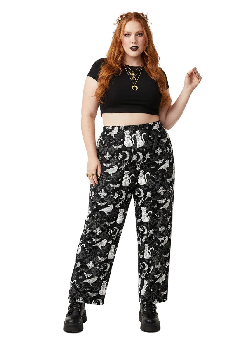 Woman wearing black wide-leg Whimsigoth lounge pants with white celestial cat and moon print.