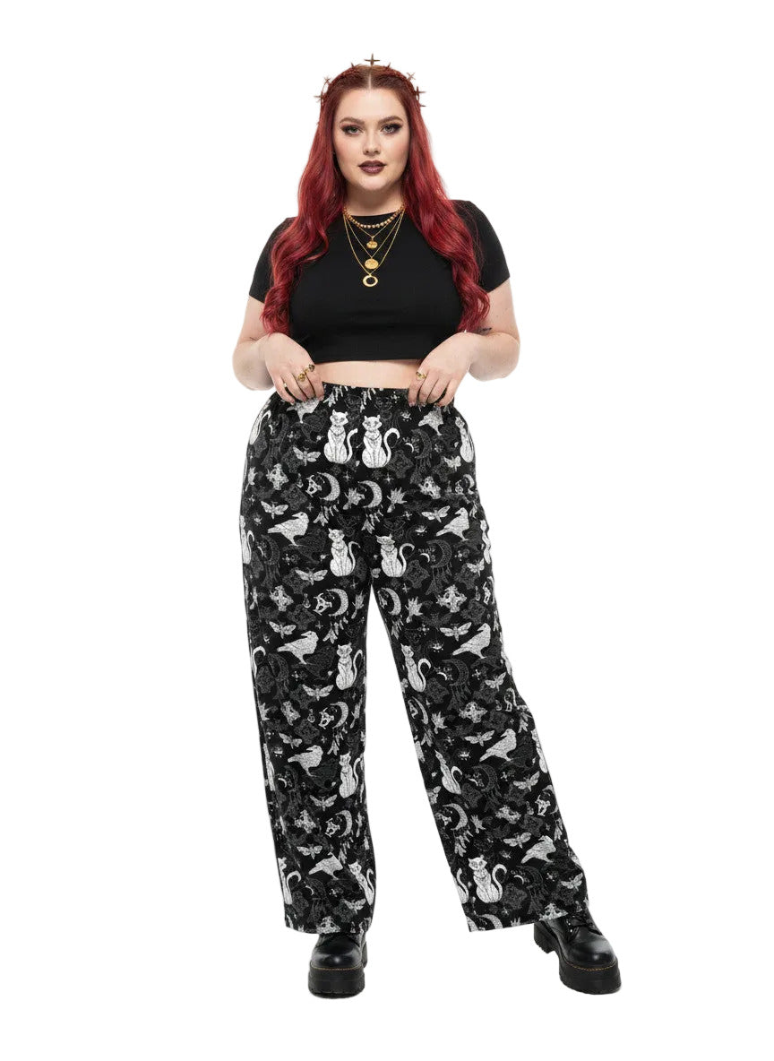 Woman wearing black wide-leg Whimsigoth lounge pants with white celestial cat and moon print.