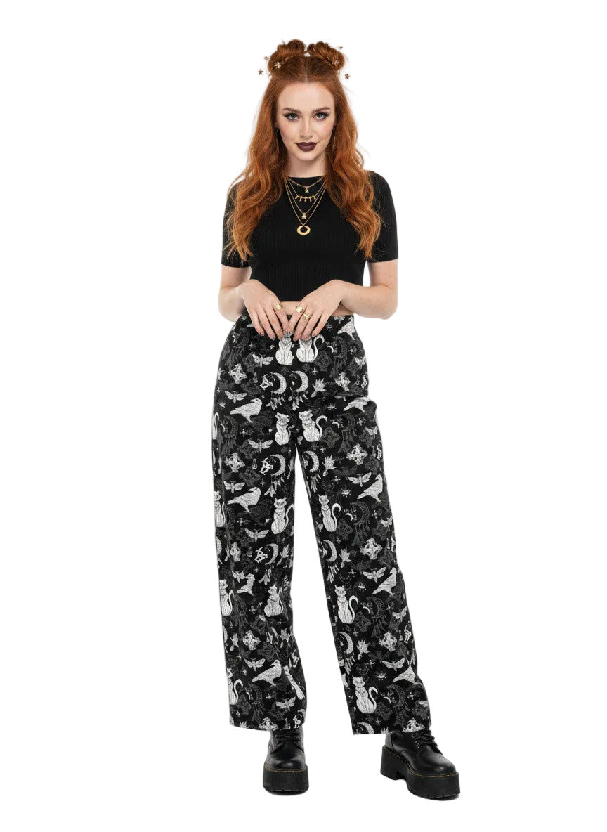 Woman wearing black wide-leg Whimsigoth lounge pants with white celestial cat and moon print.