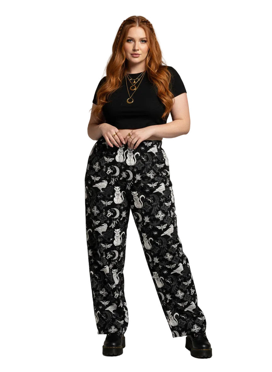 Woman wearing black wide-leg Whimsigoth lounge pants with white celestial cat and moon print.