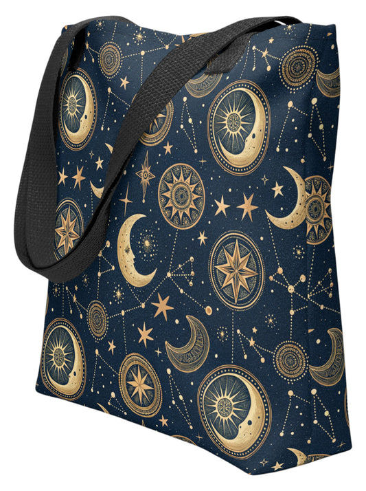 A tote bag with a dark navy blue background and a gold celestial print featuring crescent moons, stars, suns, and constellations, with black shoulder straps.