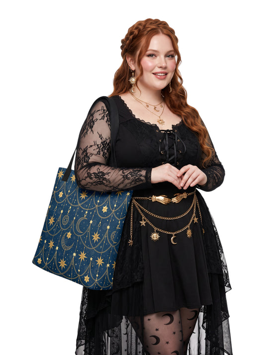 A woman with red hair models a black lace-up dress with sheer black sleeves and a gold celestial belt, carrying a blue tote bag with gold stars and moons against a white background.