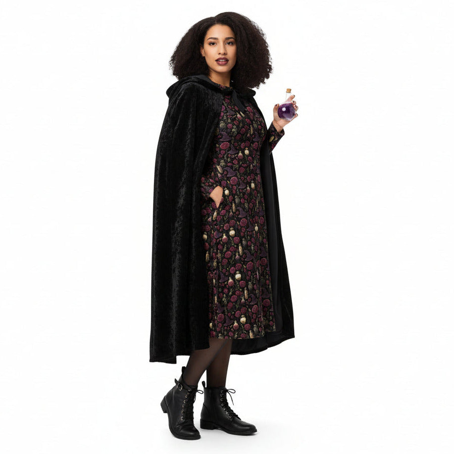 Woman wearing a black cloak over a floral dress, holding a purple potion bottle on a white background
